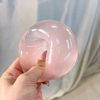Chiboki coconut oil squishy, translucent pink, held in hand with a dent from squeezing
